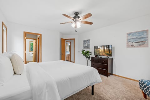 Cozy bedroom featuring a large bed, wooden dresser with TV, and decorative wall art.