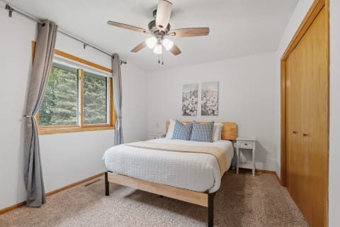 A cozy bedroom with a bed, decorative pillows, and a window with a view of trees.
