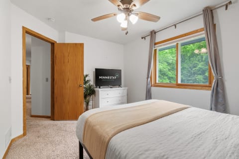 Interior view of a cozy bedroom featuring a bed, television, and window with greenery outside.