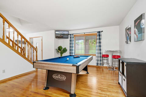A game room with a billiards table, bar stools, and decorative prints.
