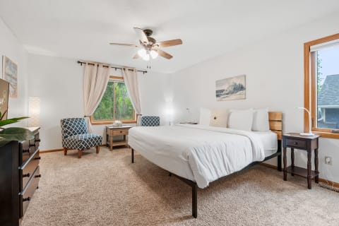A cozy bedroom featuring a bed, accent chairs, and natural light from a window.