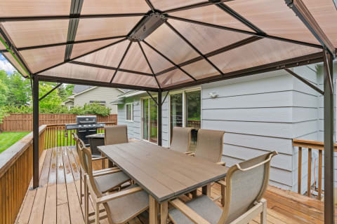 An outdoor seating area with a gazebo, dining table, and grill in a backyard.