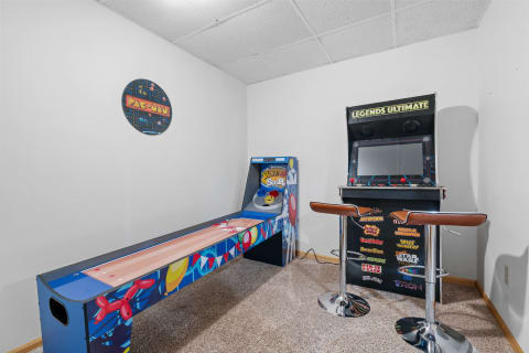 A game room with Pac-Man and Legends Ultimate arcade machines and a bar stool.