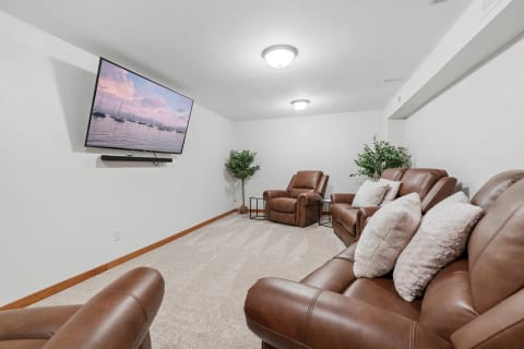 Cozy basement media room featuring a large TV and reclining chairs.