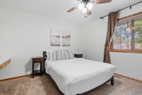 A bright bedroom featuring a double bed, nightstands, and a window with green views.