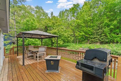 Outdoor deck with a gazebo and grill in a green backyard.
