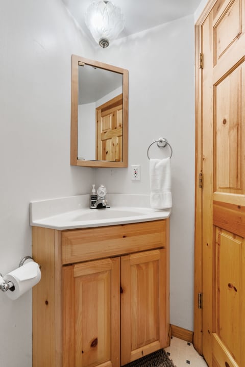Compact bathroom featuring a wooden cabinet, white sink, and ceiling light fixture.