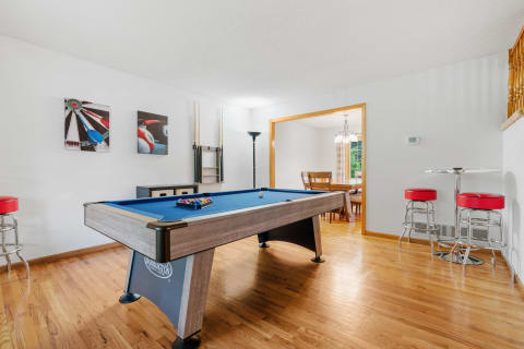 A view of a game room with a blue pool table, wall art, and a dining area in the background.
