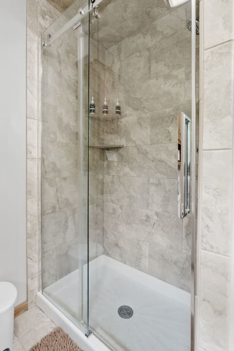 Contemporary shower with glass doors, gray tiles, and organized toiletries.
