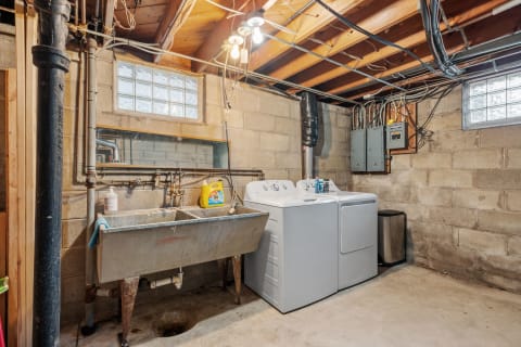 Interior view of a basement laundry space featuring washing machines and a utility sink.