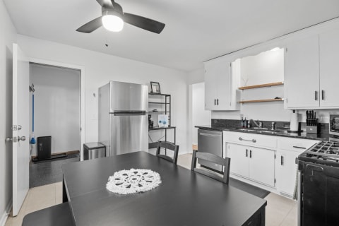 Modern kitchen with black dining table, stainless steel refrigerator, and white cabinetry.