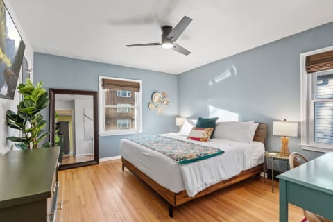A cozy bedroom featuring a bed with a floral bedspread, light blue walls, and a decorative mirror.