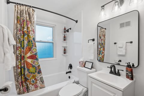 A colorful bathroom with a floral shower curtain and white fixtures.
