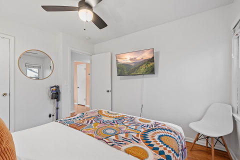 A bedroom featuring a vibrant quilt, a ceiling fan, and a mounted television.