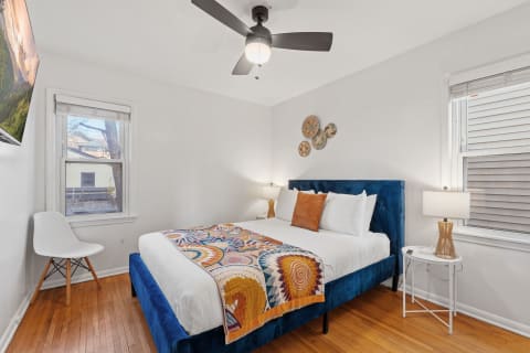 A modern bedroom with a blue velvet bed, colorful throw blanket, and a side table with a lamp.