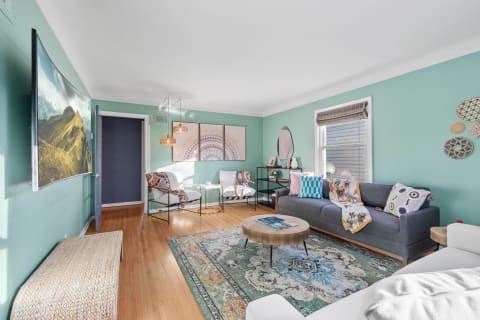 Stylish living room featuring a gray sofa, colorful pillows, and a large curved TV on mint green walls.