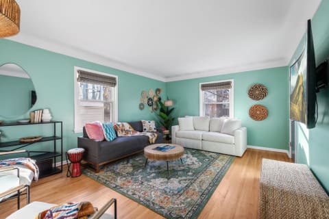 A living room featuring mint-green walls, a gray couch, white sofa, and vibrant decor.