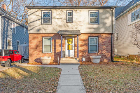 Front view of a two-story brick and stucco house with a red Jeep parked beside it.
