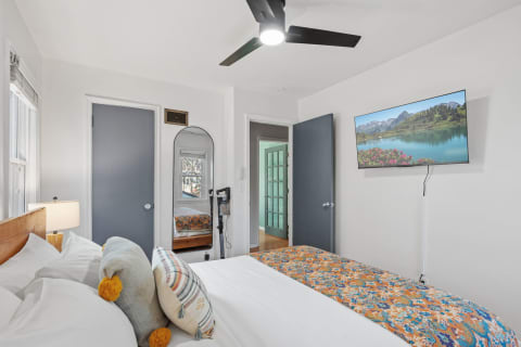 A cozy bedroom featuring a comfortable bed with a colorful throw, a ceiling fan, and a TV displaying a scenic landscape.