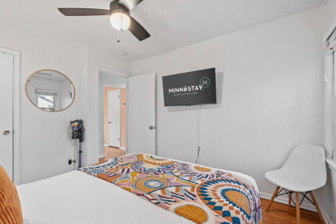 Interior view of a modern bedroom with a colorful blanket, ceiling fan, and flat-screen TV.
