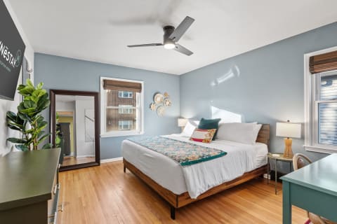 A cozy bedroom featuring a wooden bed, teal and floral pillows, a green bedside table, and a large mirror.