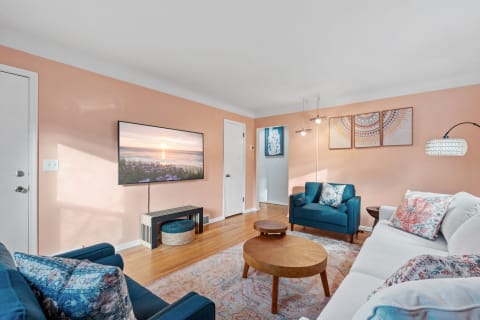 A modern living room with a peach wall, teal furniture, and a sunset image on the TV.