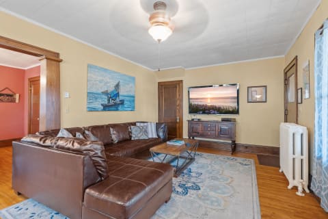 A warm living room featuring a leather sofa, wooden furniture, and a scenic painting.