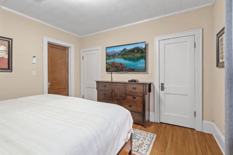 A bedroom with a bed, wooden dresser, and a TV displaying a scenic landscape.
