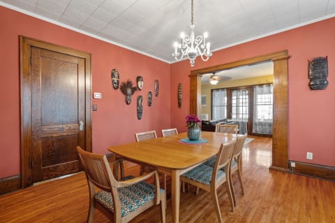 A warm dining room with a wooden table, colorful chairs, and cultural masks on the wall.