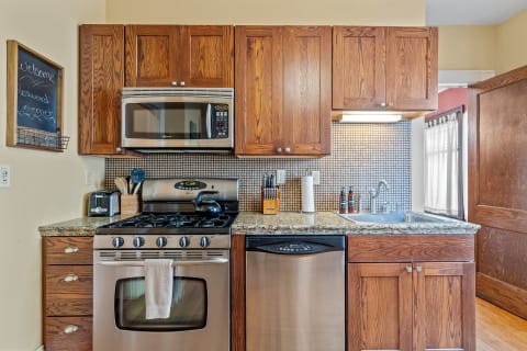 Cozy kitchen featuring wooden cabinets and stainless steel appliances, with a granite countertop and chalkboard sign.