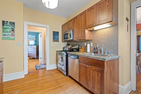 Interior view of a warm kitchen featuring wooden cabinets, granite countertops, and stainless steel appliances.