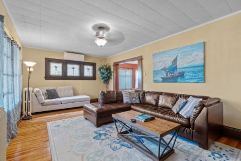 A cozy living room featuring a leather sectional sofa, a coffee table, ocean-themed artwork, and stained glass windows.