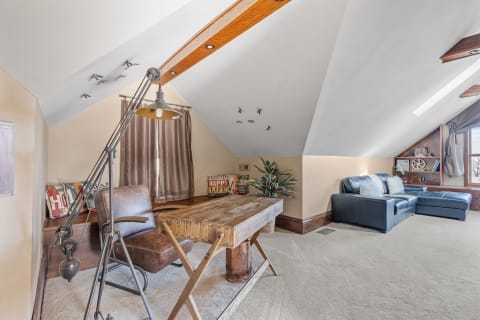 Attic workspace featuring a rustic wooden desk, leather chair, and a blue sectional couch.