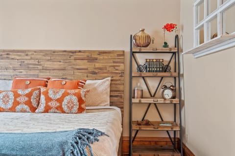 Cozy bedroom featuring wooden headboard, colorful pillows, and a stylish bookshelf.
