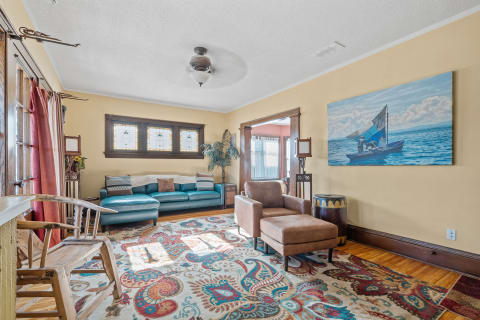Bright living room with teal sofa, leather chair, colorful rug, and coastal artwork.
