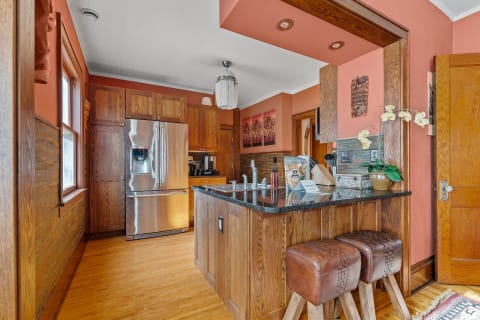 Stylish kitchen with oak cabinetry, granite countertops, and modern appliances, featuring leather stools.