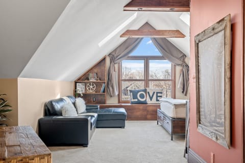Attic interior with a leather sofa, a window seat, and a wooden bookcase under sloped ceilings.