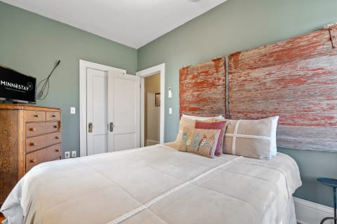 Cozy bedroom featuring sage green walls, a rustic wooden headboard, and decorative pillows.