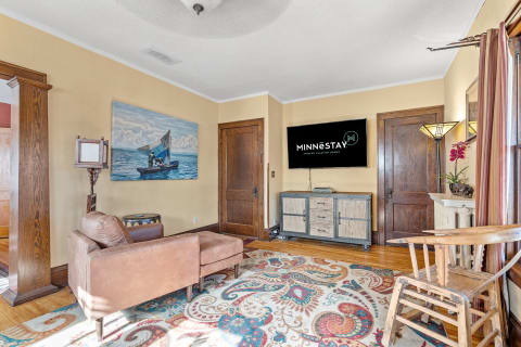 A living room with a brown sofa, decorative rug, large painting, and mounted TV.