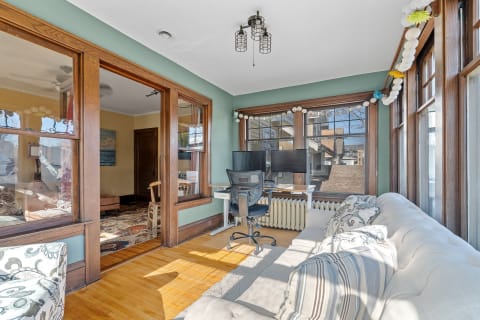 Sunroom with large windows, a white sofa, and a workspace with dual monitors.