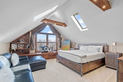 A bright and cozy attic bedroom featuring a bed, leather sofa, and artistic decor.