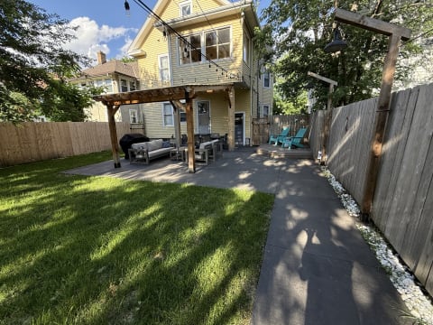 Backyard of a yellow house featuring a seating area and a pathway bordered with pebbles.