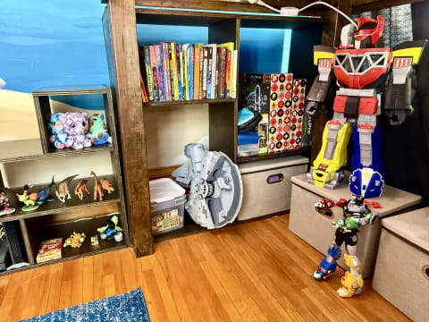 A playful corner in a room featuring a large robot toy, shelves with books, and various toy figures.