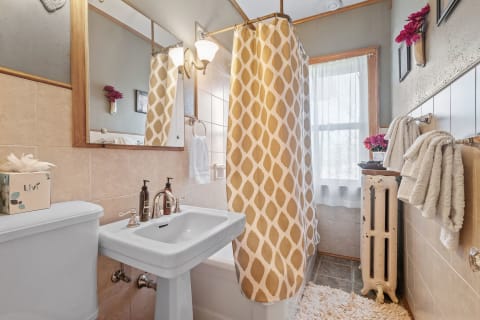 A stylish bathroom featuring a white sink, patterned shower curtain, and warm decor.
