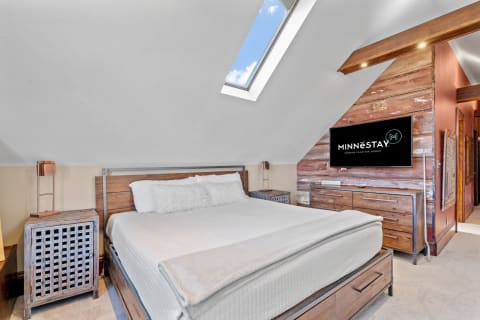 A modern attic bedroom with a wooden bed, stylish lamp, and a skylight.