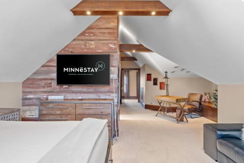 A cozy attic room with wooden accents, a TV, and a small desk.