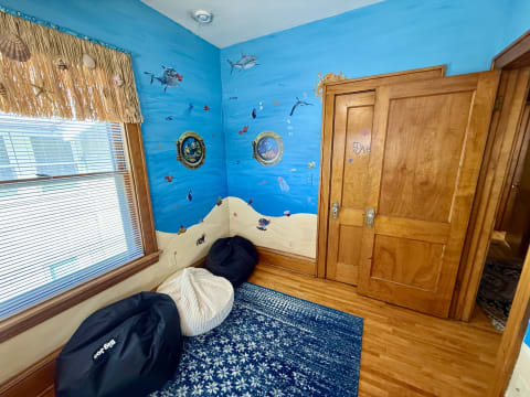 A corner of a room featuring vibrant ocean murals, porthole frames, black bean bag chairs, and wooden trim.