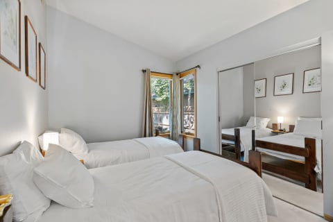 A simple bedroom with two twin beds, framed artwork, and large windows.