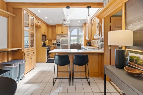 A bright kitchen featuring oak cabinets, bar stools, and stainless steel appliances.
