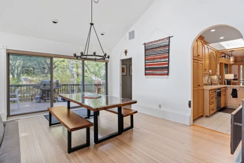 Spacious dining room with wooden table, benches, and a view of a deck through glass doors.